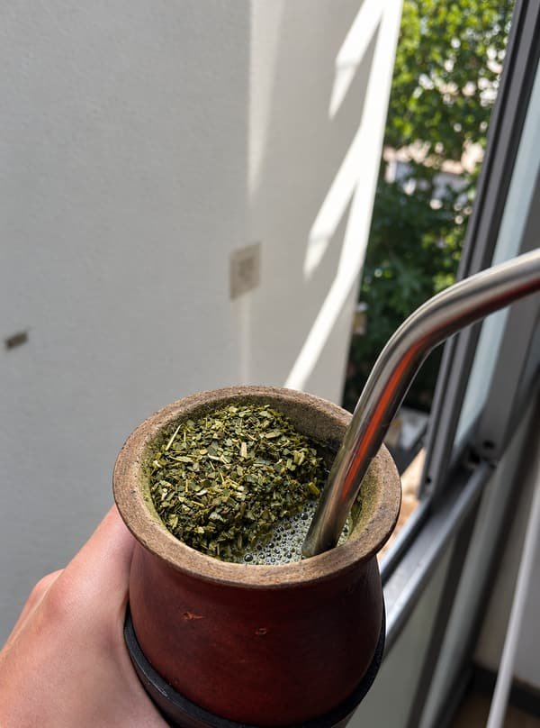 Mate con yerba de molienda fina y bombilla de acero, junto a una ventana.