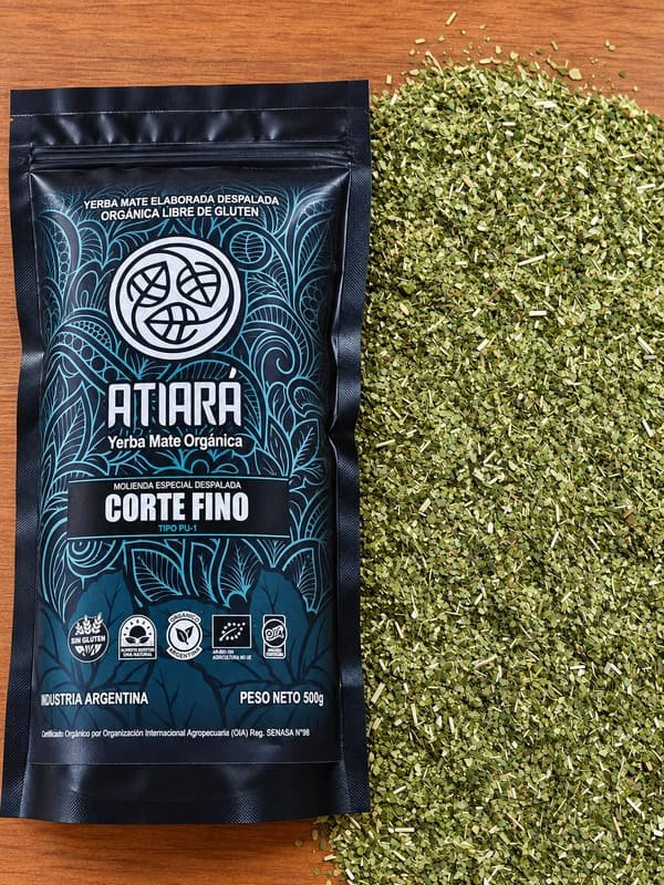 Paquete de Atiará Corte Fino junto a una pila de yerba de molienda fina, sobre una mesa de madera.