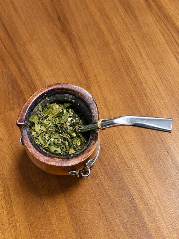 Mate de madera con yerba de hojas grandes y bombilla de acero, visto desde arriba.
